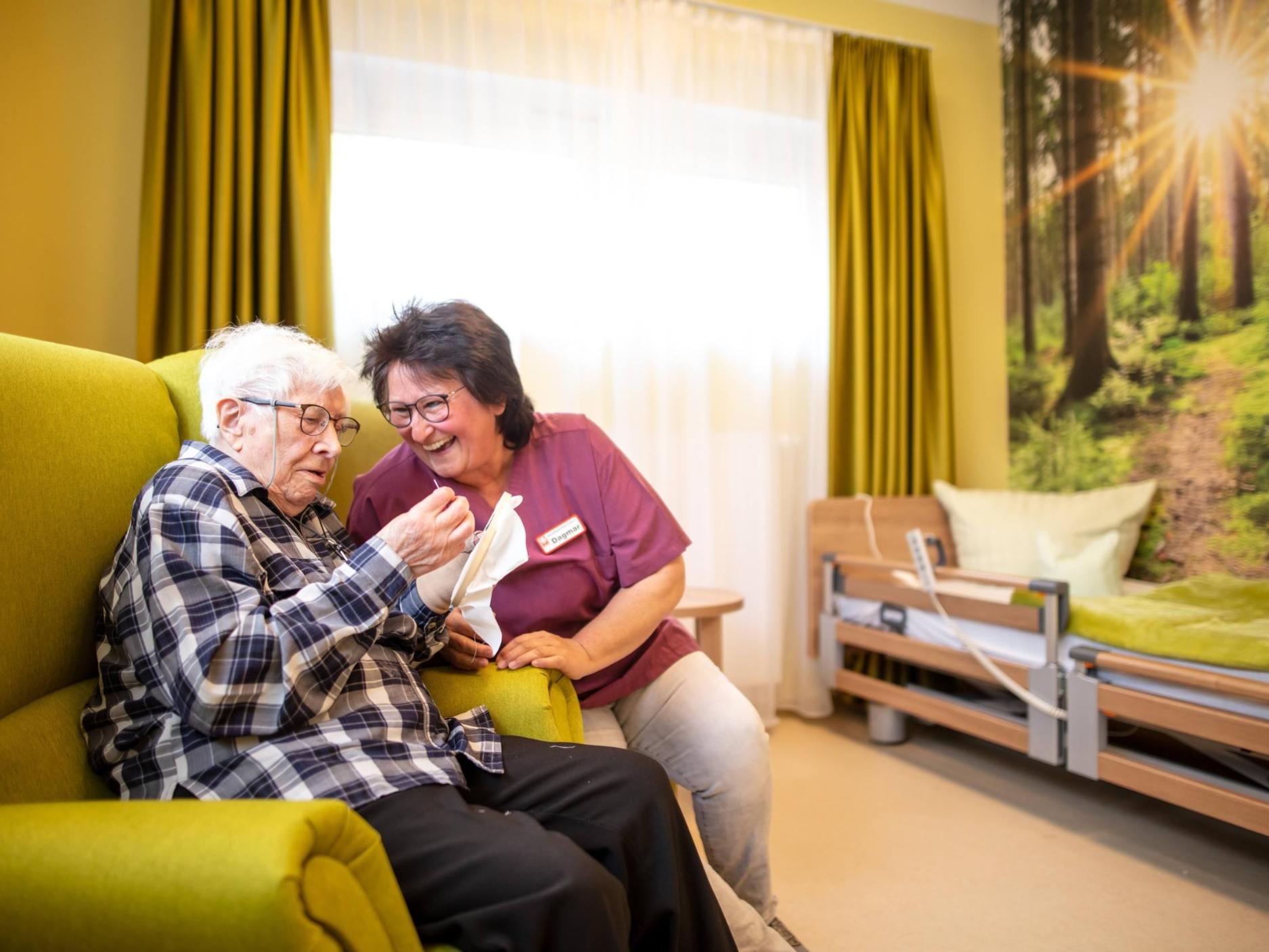 Eine Seniorin sitzt im Sessel und lässt sich unterhalten.
