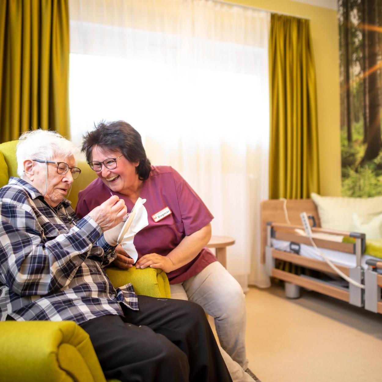 Eine Seniorin sitzt im Sessel und lässt sich unterhalten.