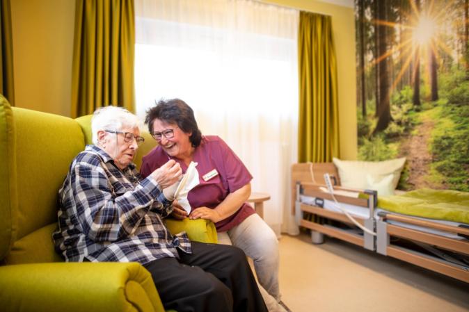 Eine Seniorin sitzt im Sessel und lässt sich unterhalten.